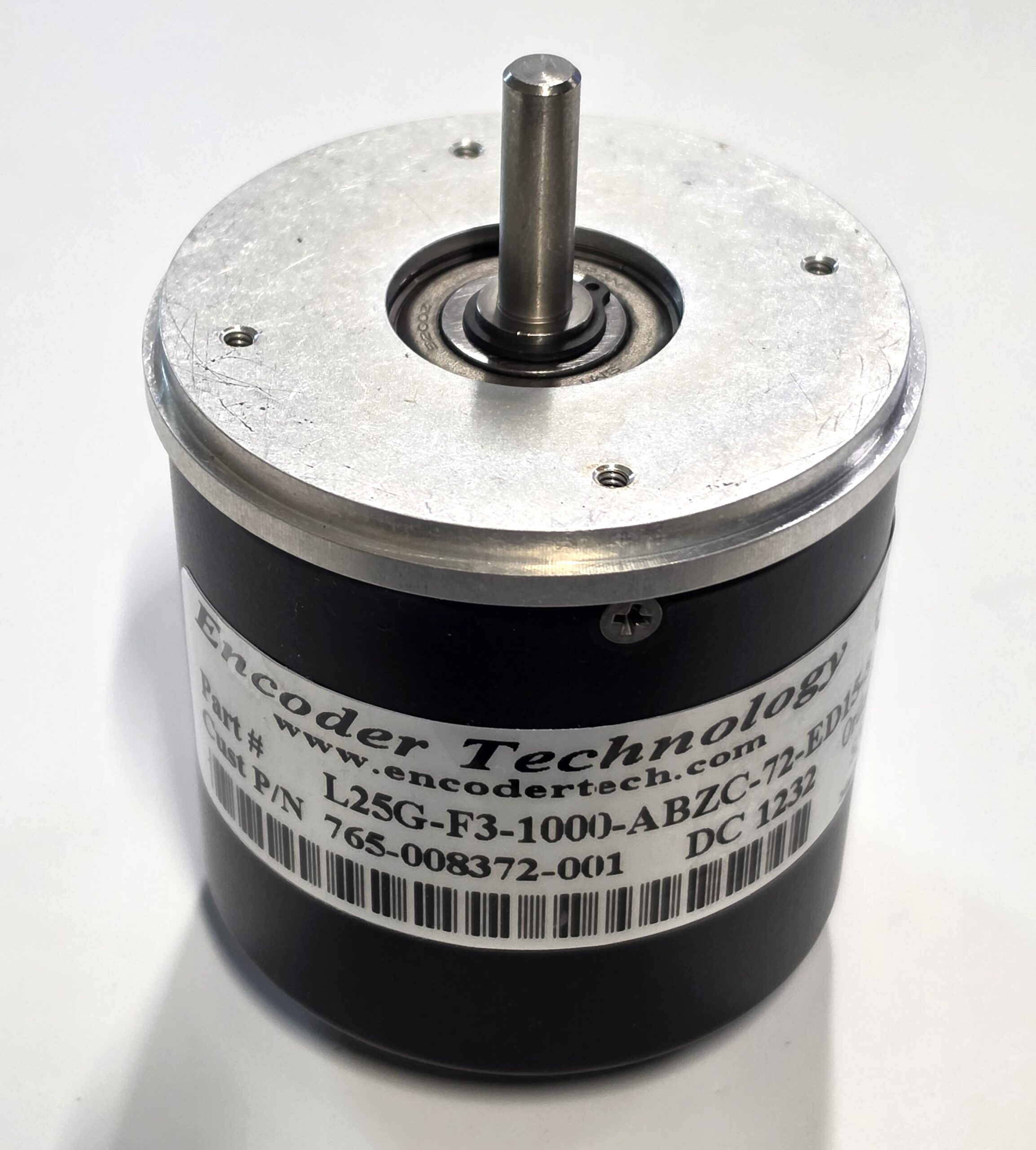 Close-up of a cylindrical DC motor with a vertical drive shaft and a silver bearing housing in the center of a metal top plate.
