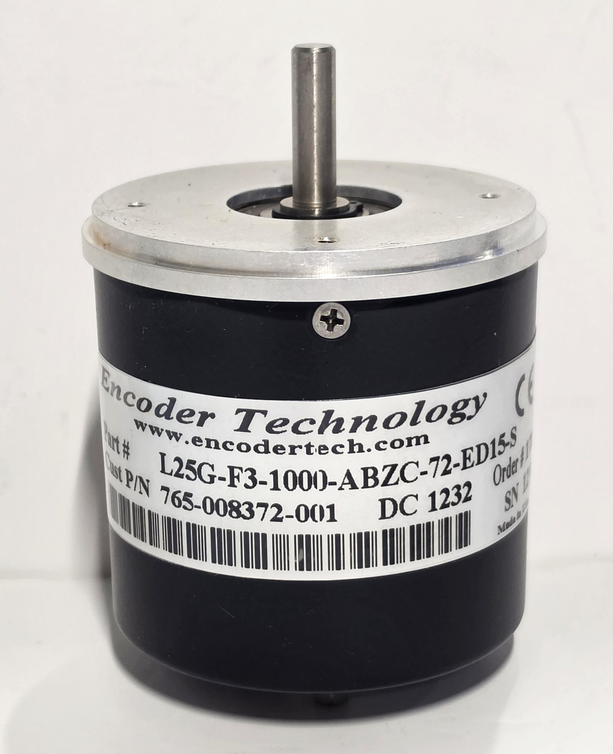 Close-up of an encoder with a metal shaft protruding from a black cylindrical housing and a barcode label nearby on the side of the device.