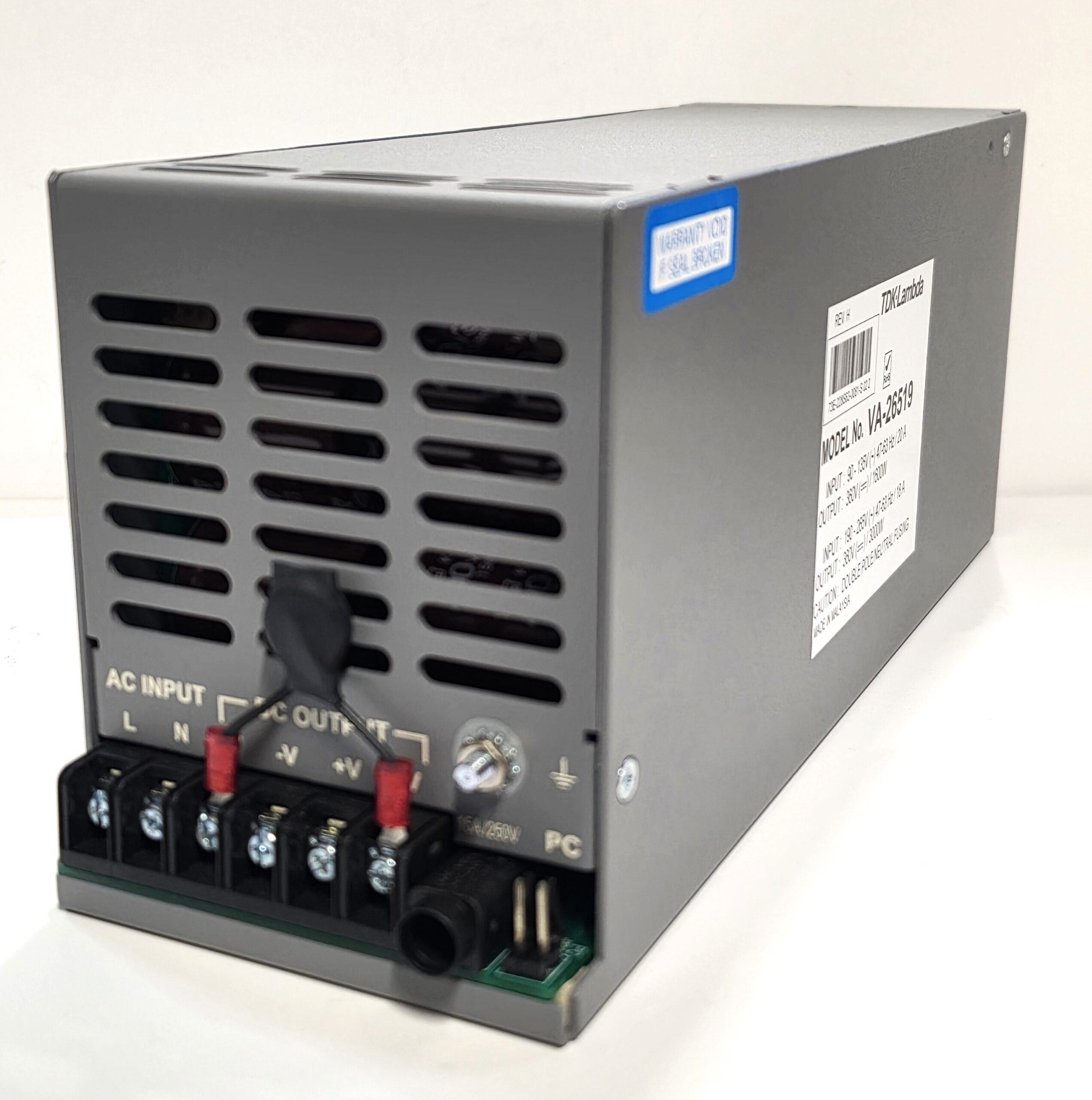 Gray metal power supply unit with vented sides; front terminal block and red jumpers visible, plus a side label with model number VA-26519