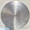 Close-up of a circular brushed-metal perforated plate (speaker/grill) with tiny evenly spaced holes and small mounting holes around the edge, text at top reads 'Made in Singapore'.