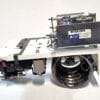 Close-up of a precision lab/industrial device with a large wheel, metal housing, and exposed wiring on a white surface