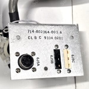 Close-up of a silver metal electrical component with a six-pin circular connector and stamped part numbers 714-802364-003 A and 9334 0201.