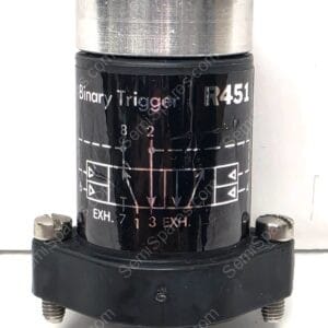 Close-up of a black cylindrical device labeled 'Binary Trigger' with a silver top and mounting studs on the bottom edge.