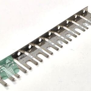 Metal gauge/ruler strip with multiple forked tines and circular holes, laid diagonally on a white background.