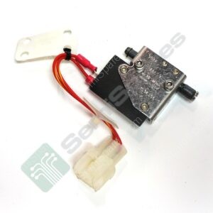 Close-up of a small black electrical component with red wires attached and a white mounting plate nearby